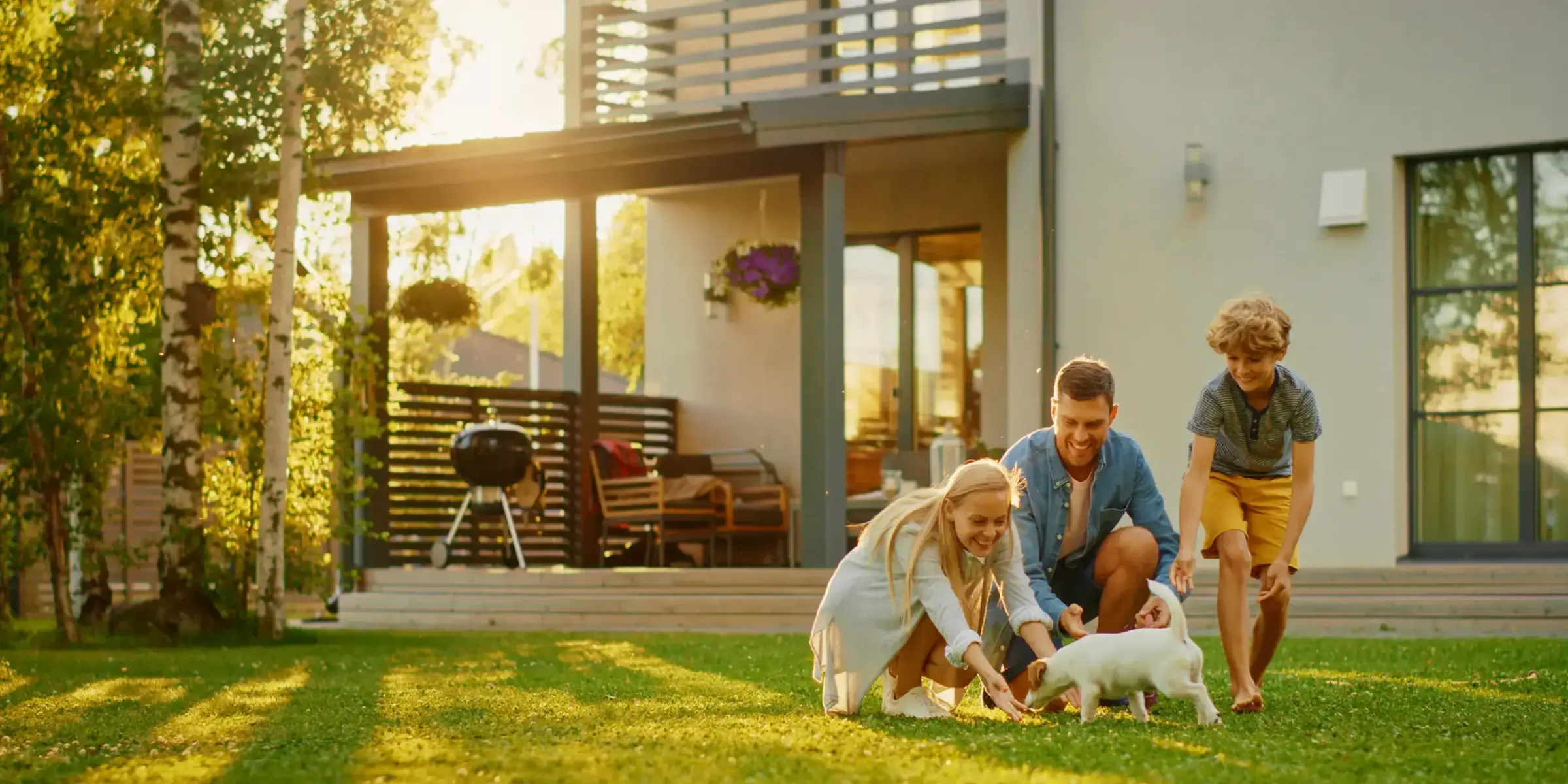 Smiling Father, Mother and Son Pet and Play with Smooth Fox Terrier Retriever Dog. Sun Shines on Idyllic Happy Family with Loyal Pedigree Dog have Fun at the Idyllic Suburban House Backyard