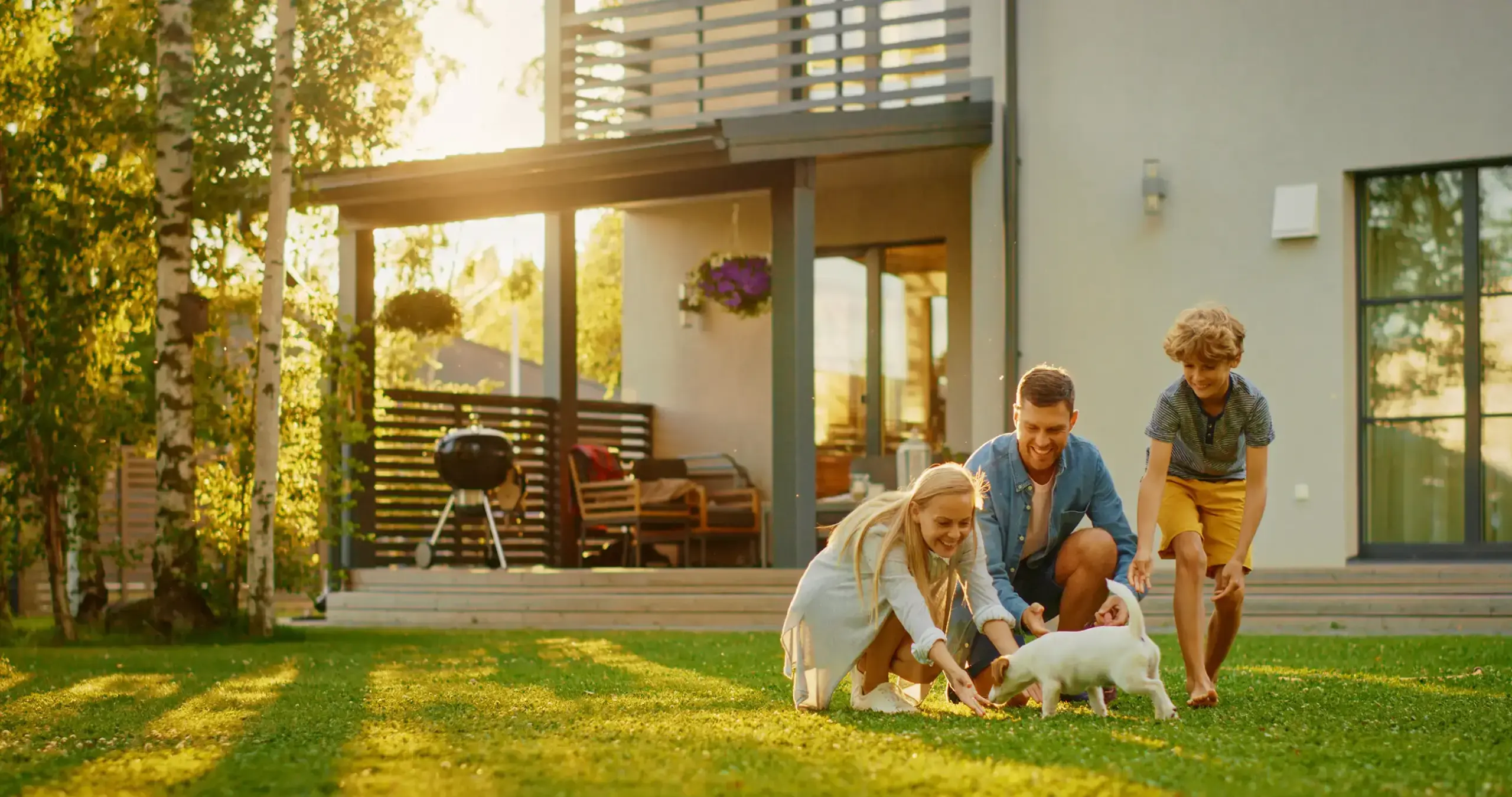 Smiling Father, Mother and Son Pet and Play with Smooth Fox Terrier Retriever Dog. Sun Shines on Idyllic Happy Family with Loyal Pedigree Dog have Fun at the Idyllic Suburban House Backyard